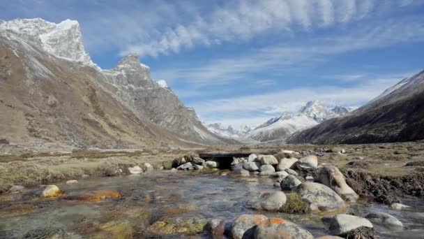 Corriente de aguas poco profundas murmullo alrededor de piedras por montañas nevadas bajo el cielo azul — Vídeo de stock