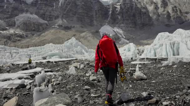 Alpinist mit rotem Rucksack wandert auf felsigem Pfad entlang des Gletschers zum Everest Base Camp — Stockvideo