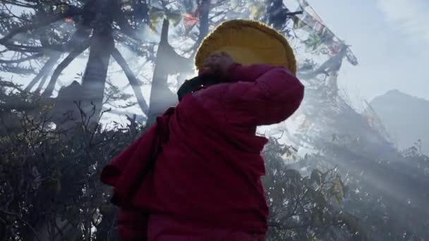El monje budista con túnica roja se quita el sombrero amarillo. Sol brilla en densa niebla humeante — Vídeos de Stock