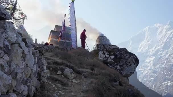 Буддийский монах разжигает огонь снаружи храма, густо курит вокруг снежных гор — стоковое видео