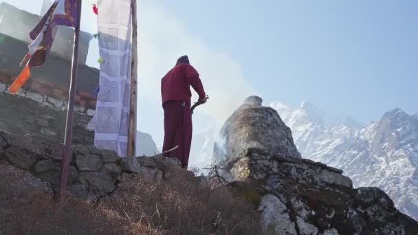 A buddhista szerzetes tüzet gyújt a templom előtt. A füst feljebb megy. Hó hegyek háttér — Stock videók