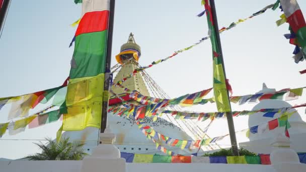 Wielokolorowe flagi modlitewne trzepoczą w pobliżu złotej białej świątecznej Swayambhunath stupa — Wideo stockowe