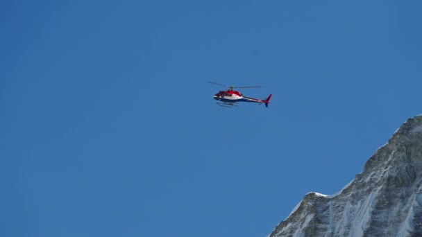 Helikopter penyelamat terbang tinggi di langit biru di atas pegunungan bersalju di bawah sinar matahari — Stok Video
