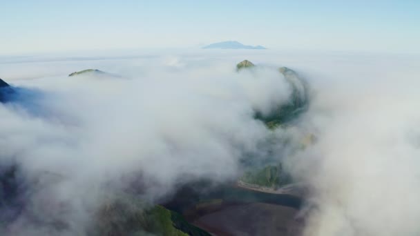Vuelo sobre densas nubes blancas sobre aguas oscuras con verdes colinas en la costa — Vídeos de Stock