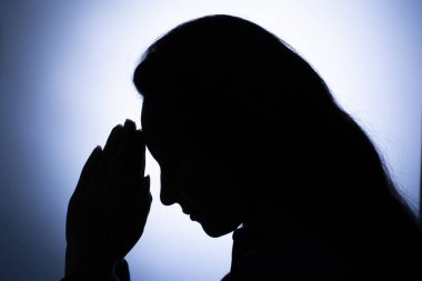 Bir kadının silueti ışığa karşı dua ediyor.