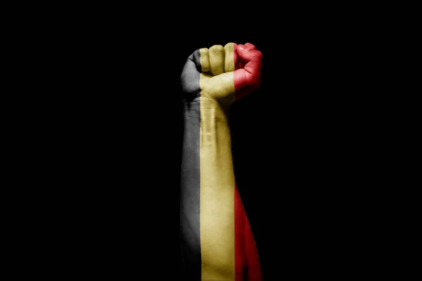 Strong man\'s hand in battle signal with Belgium flag on black background.