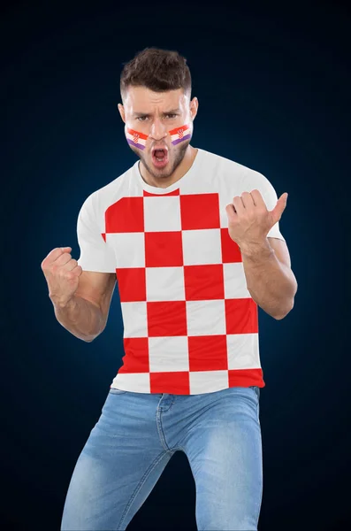 Soccer fan man with jersey and face painted with the flag of the Croatia team screaming with emotion on black background.