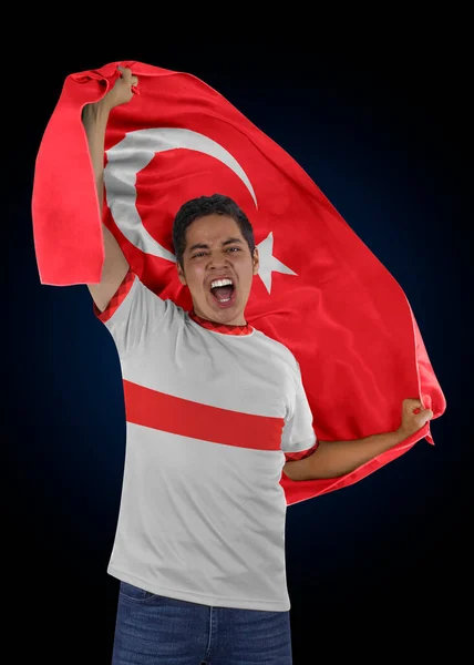 Soccer fan with the flag of his country Turkey and jersey shouting with emotion for the victory of his team on a black background.