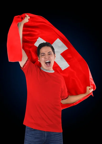 Soccer fan with the flag of his country Switzerland and jersey shouting with emotion for the victory of his team on a black background.