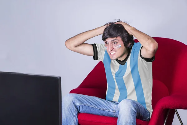 Miłośnik Piłki Nożnej Ogląda Telewizję Koszulką Twarzą Pomalowaną Flagą Argentyny — Zdjęcie stockowe