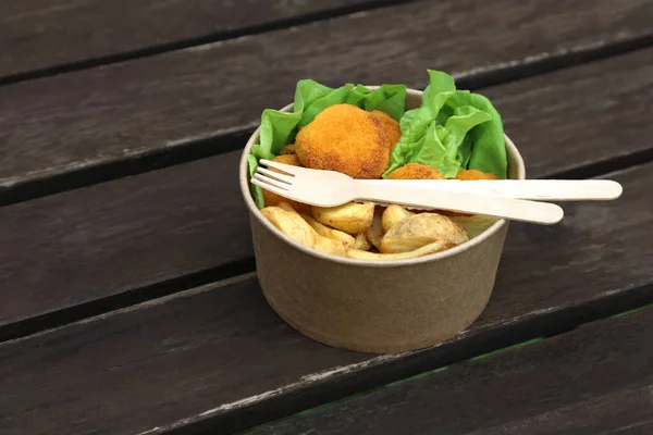 Food takeout concept, meal in kraft disposable bowl on wooden table with disposable wooden cutlery. Environmentally friendly.