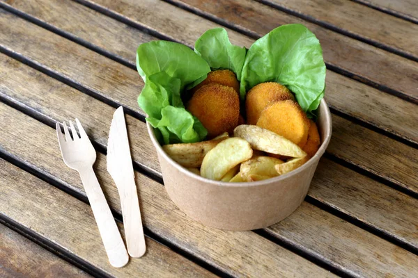 Food takeout concept, meal in kraft disposable bowl on wooden table with disposable wooden cutlery. Environmentally friendly.