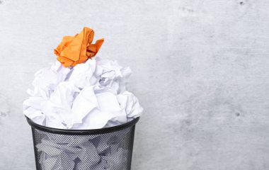 Crumpled white paper in the trash can, and orange paper ball on the top