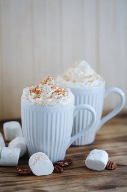 Delicious latte with whipped cream and powder on top and marshmallow on the table