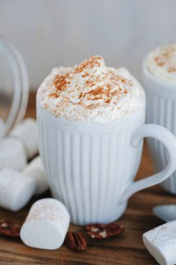 Delicious latte with whipped cream and powder on top and marshmallow on the table