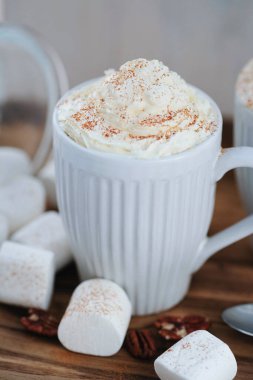 Delicious latte with whipped cream and powder on top and marshmallow on the table