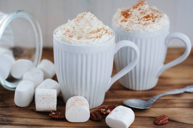 Delicious latte with whipped cream and powder on top and marshmallow on the table