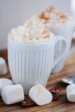 Delicious latte with whipped cream and powder on top and marshmallow on the table