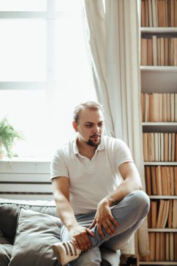 Yakışıklı adam evdeki kanepede oturuyor.