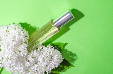 Beyaz leylak çiçekleri ve yeşil arka planda parfümlü bir şişe. Parlak gölgeler ve ışık. Metnin için yer.