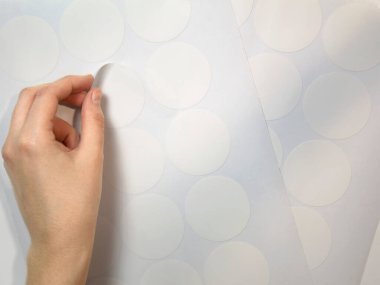 Düzenli bir kadın eli, entrikacının budadığı yuvarlak beyaz etiketi soyar. Model etiketleri