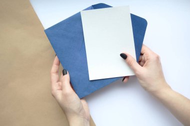 Beyaz çarşaf ve mavi zarfı kahverengi ve beyaz arka planda tutan manikürlü kadın elleri. Kartpostal düzeni