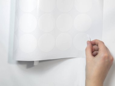 Düzenli bir kadın eli, entrikacının budadığı yuvarlak beyaz etiketi soyar. Model etiketleri