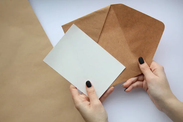 女性的手 修指甲时 手托着一张白色的床单和一个棕色的信封 垂直地放在棕色和白色的背景上 明信片的布局 — 图库照片