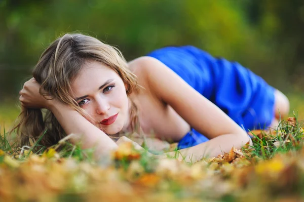 Meisje in een blauwe jurk op gele bladeren — Stockfoto