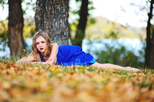 Mädchen im blauen Kleid auf gelben Blättern — Stockfoto