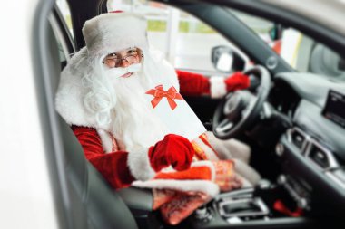 Noel Baba, yeni bir arabanın kabininde, direksiyonda oturuyor, gülümsüyor ve elinde beyaz bir çarşaf tutuyor..