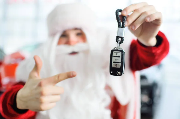 Papai Noel está sorrindo enquanto segura as chaves de um carro novo. — Fotografia de Stock