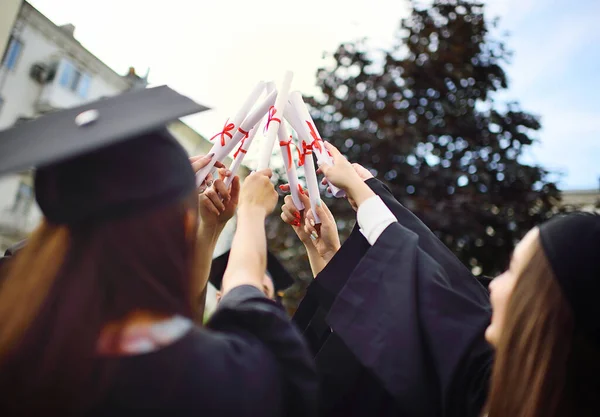 Grupo de graduados universitários em vestes de estudante ou manto e chapéus quadrados na cerimônia de formatura realizar certificados de graduação da faculdade em suas mãos e se alegrar. — Fotografia de Stock
