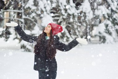 Güzel kız gülümsüyor, eğleniyor ve kış ormanlarının ve karla kaplı ağaçların arkasına kar atıyor. Kış eğlencesi
