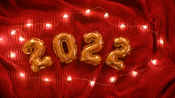 Αριθμοί 2022 στο φόντο του ένα κόκκινο πλεκτό άνετο καρό και χριστουγεννιάτικα φώτα. — Αρχείο Βίντεο