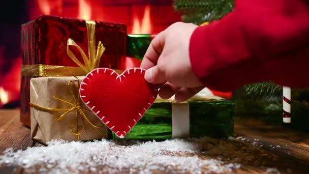 Een close-up van een mans hand in een rode hoodie zet een rood vilten hart en een valentijnboodschap "With Love" op een houten tafel — Stockvideo