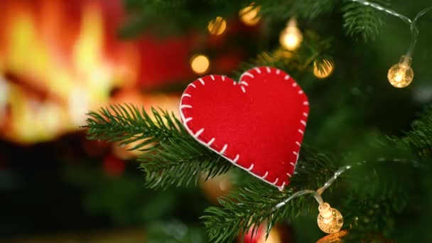 Een close-up van een hand zet een briefje met de tekst "With Love" op de kerstboom naast een rood vilten hart op de achtergrond van de open haard. — Stockvideo