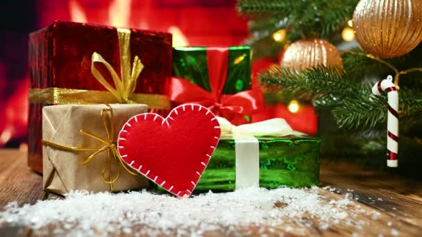 Een rood vilten hart op de achtergrond van een brandende open haard, een versierde kerstboom en geschenken. — Stockvideo