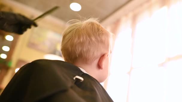 Barber makes the first haircut for a one-year-old child in a modern barbershop. Childrens haircut — Vídeo de Stock