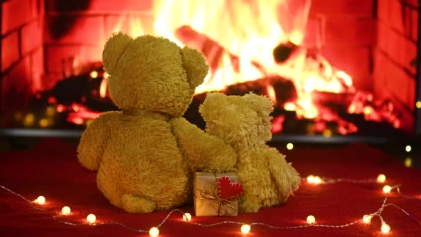 Pair of teddy bears are sitting hugging against the background of the fireplace and holding in their paws a box with a gift and a red heart. Valentines Day — 비디오