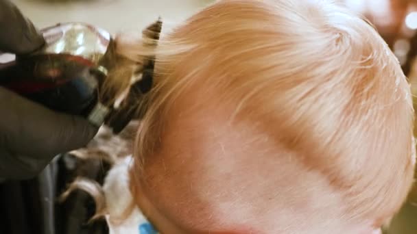 Berber, modern bir berber dükkanında bir yaşındaki bir çocuğun saçını ilk kez kesiyor. Çocukların saç kesimi — Stok video