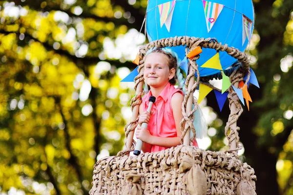 Little girl in pink clothes with a telescope in her hands in the basket of a blue balloon looks into the distance and smiles. — Stock Photo, Image