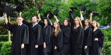Siyah cübbeli üniversite ya da üniversite mezunları mezunların kare şapkalarıyla ellerini kaldırdılar ve mezuniyetten memnunlar..