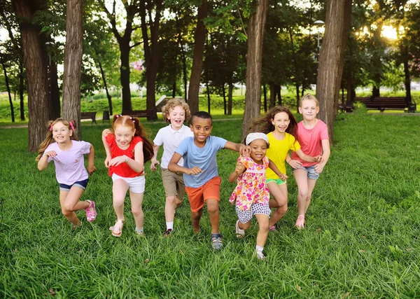 Um grupo de pré-escolares correndo na grama contra o fundo do parque e vegetação. — Fotografia de Stock