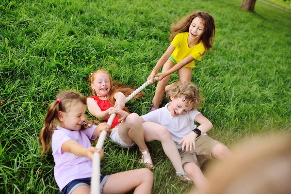 Grupo de niños en edad preescolar - niños y niñas compiten en un tira y afloja contra el fondo de un parque y vegetación. — Foto de Stock