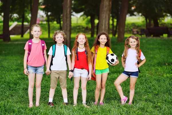 Grupo de niños con una pelota de fútbol y mochilas escolares en un fondo de vegetación y un parque. Regreso a la escuela — Foto de Stock