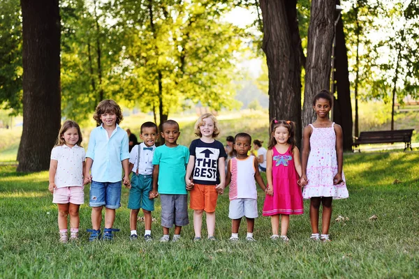 Muitas crianças de raças diferentes brincam juntas no Parque na grama fresca verde. — Fotografia de Stock