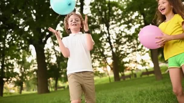 Chłopiec z kręconymi włosami i okularami bawiący się niebieskim balonem na tle zieleni i parku — Wideo stockowe