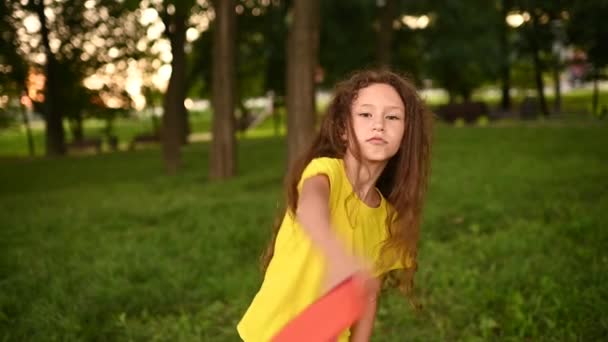 En skolflicka flicka med lockigt hår, jublar i början av semestern och kastar upp en skola ryggsäck mot bakgrund av en park och grönska. — Stockvideo