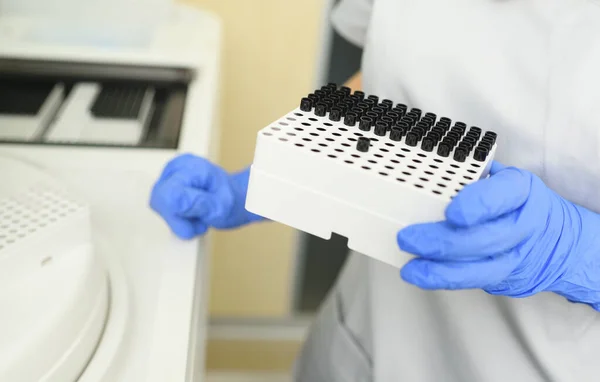 Primer plano de un empleado de un laboratorio médico bacteriológico que sostiene un recipiente con tubos de ensayo sobre el fondo del analizador. — Foto de Stock